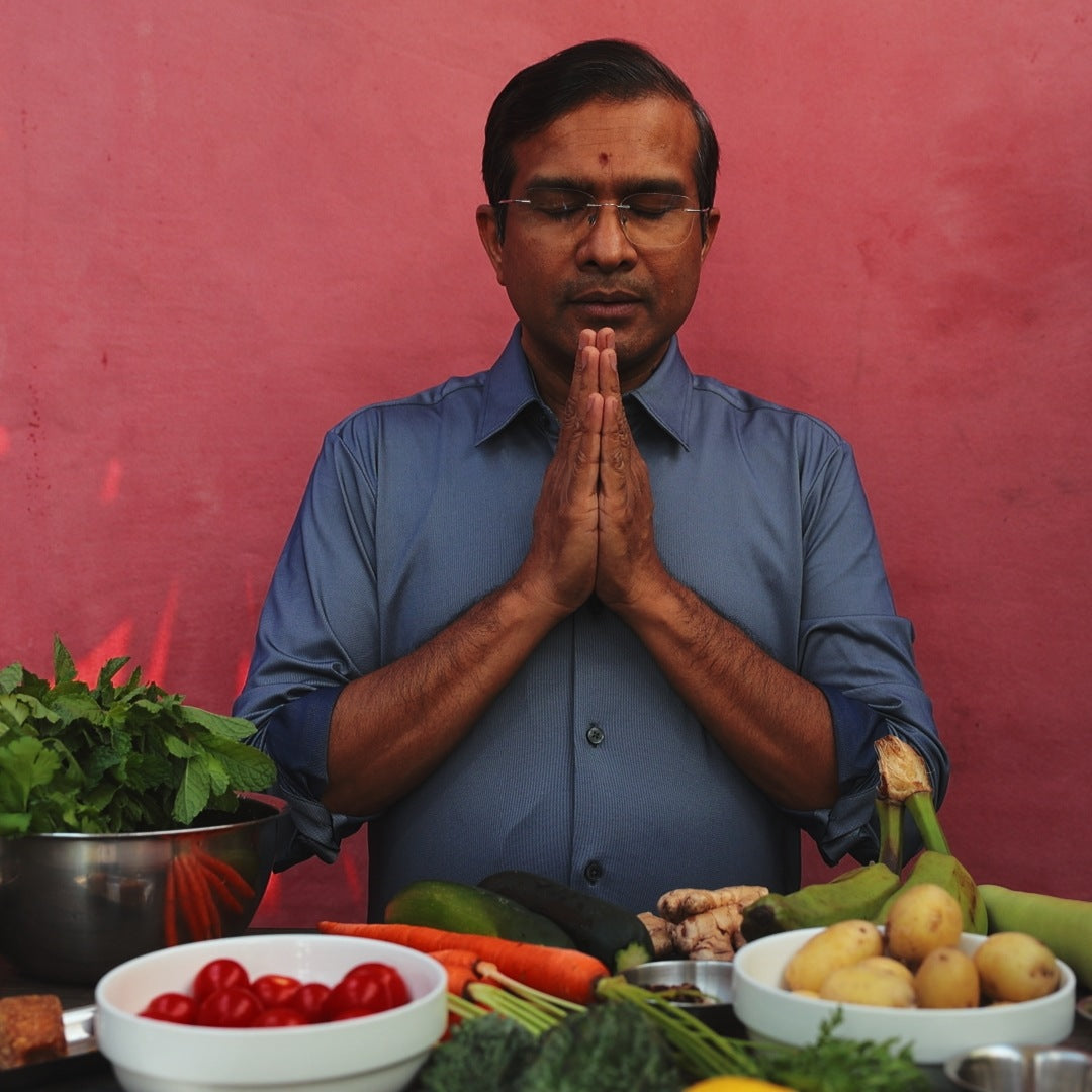Vaidya Jay in namaste at a table of vegetables, teaching the six tastes of Ayurveda