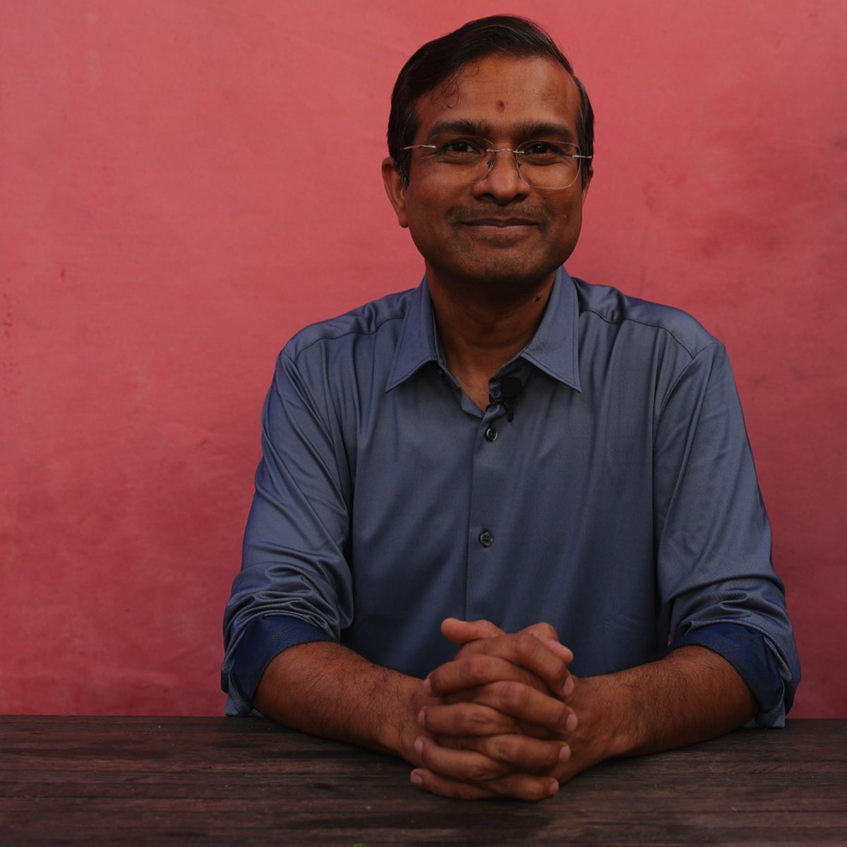 Vaidya Jay at a wooden table, hands folded, answering an audience question about food combining