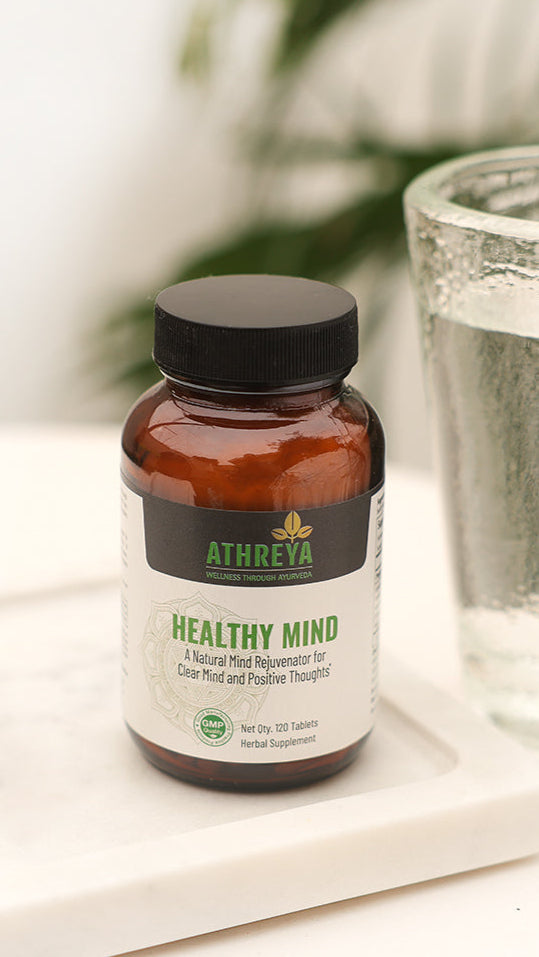 A bottle of Athenea Healthy Mind supplement with capsules and a glass of water on a white surface.