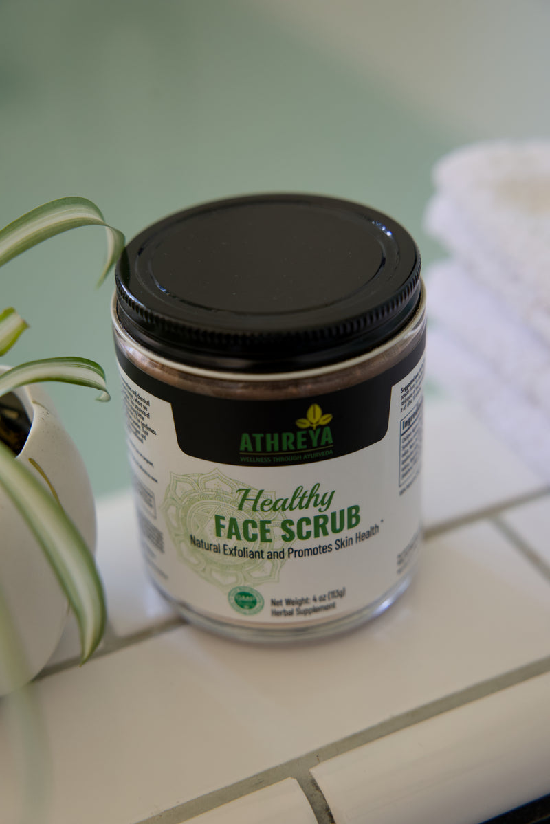 Athreya Healthy Face Scrub jar on a bathroom counter with a plant and towel in the background.